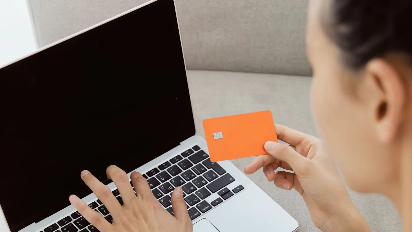A woman holding a bank card while typing on a laptop at home
