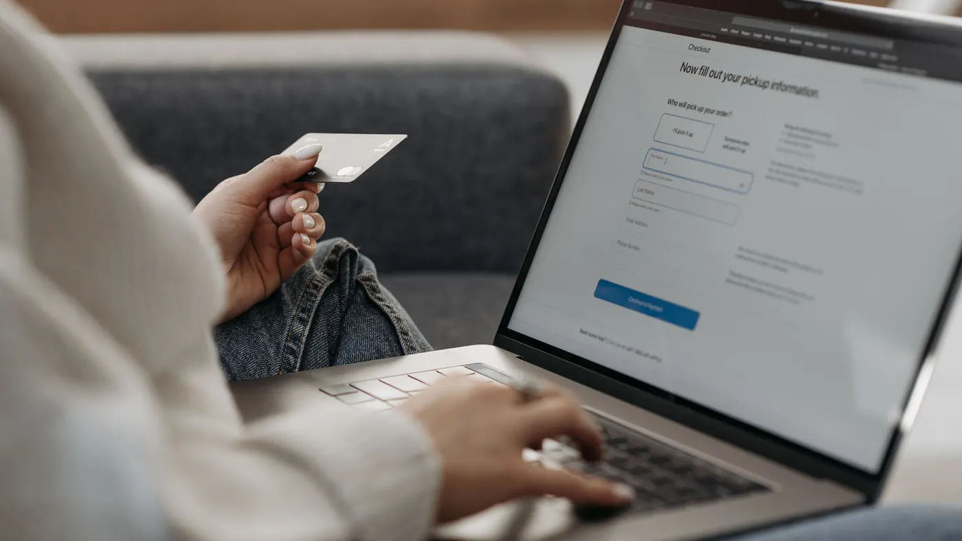 A woman on a sofa holding a bank card while paying on her laptop