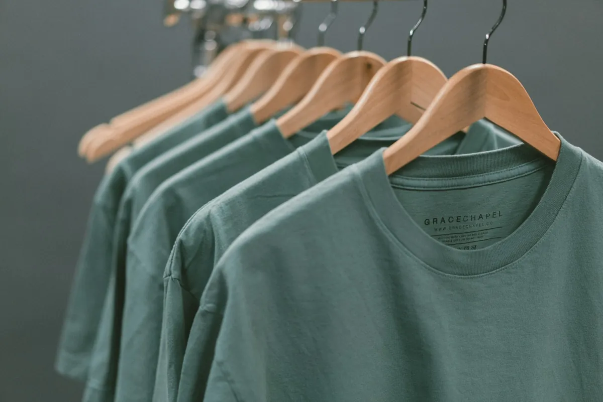 Sage-green t-shirts on wooden hangers in a manufacturing studio