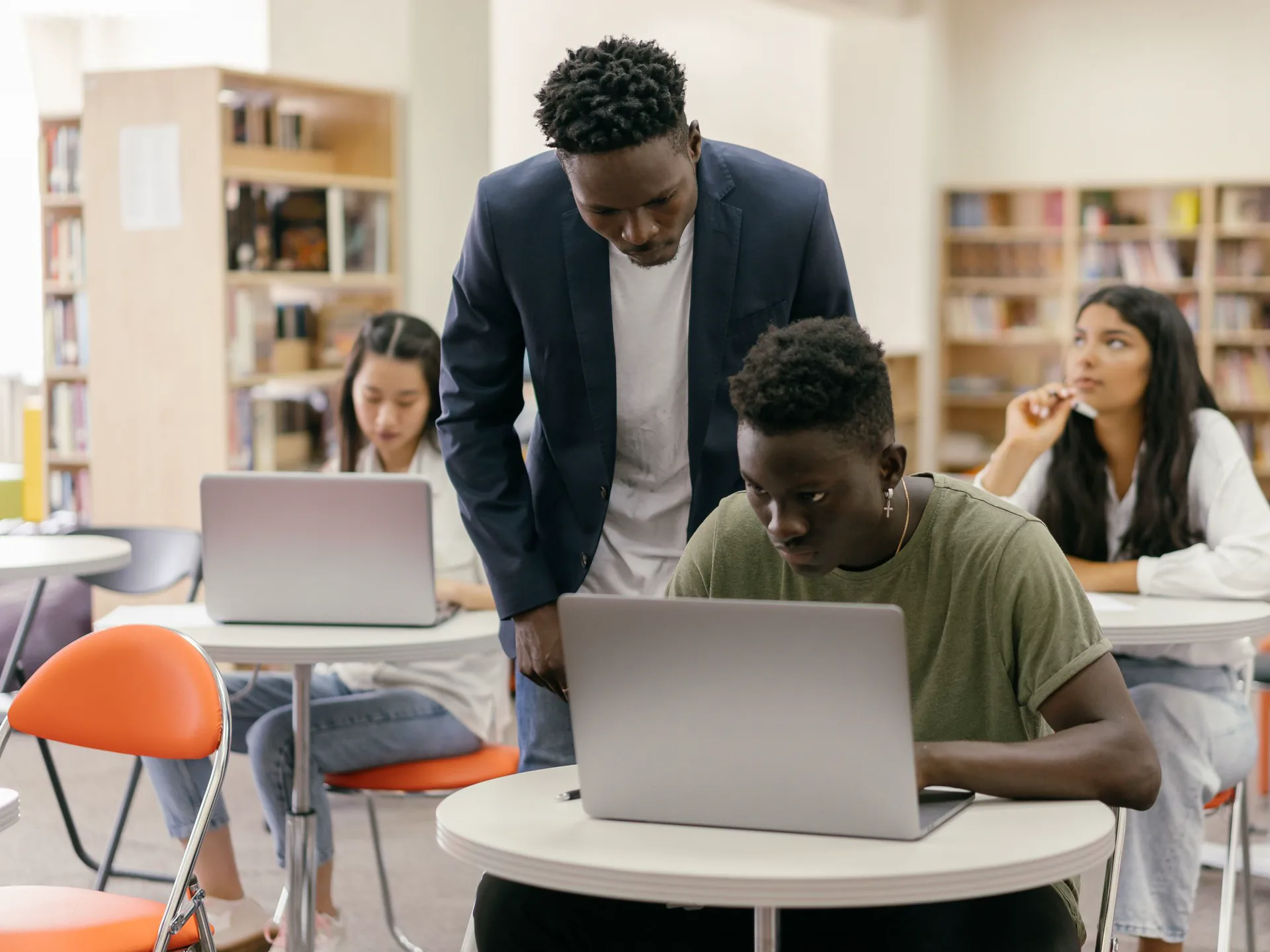 A teacher guiding students working on laptops in a modern campus library
