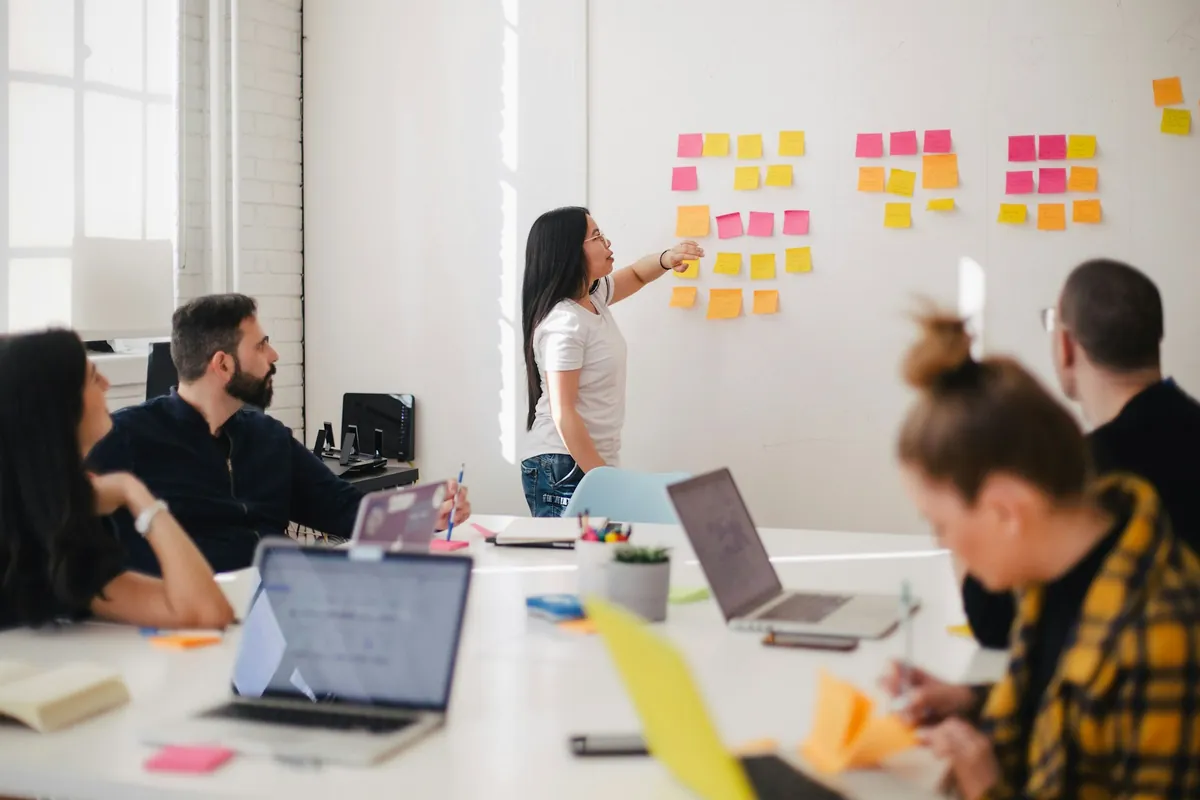 A team in a meeting room reviewing a board of colourful sticky notes