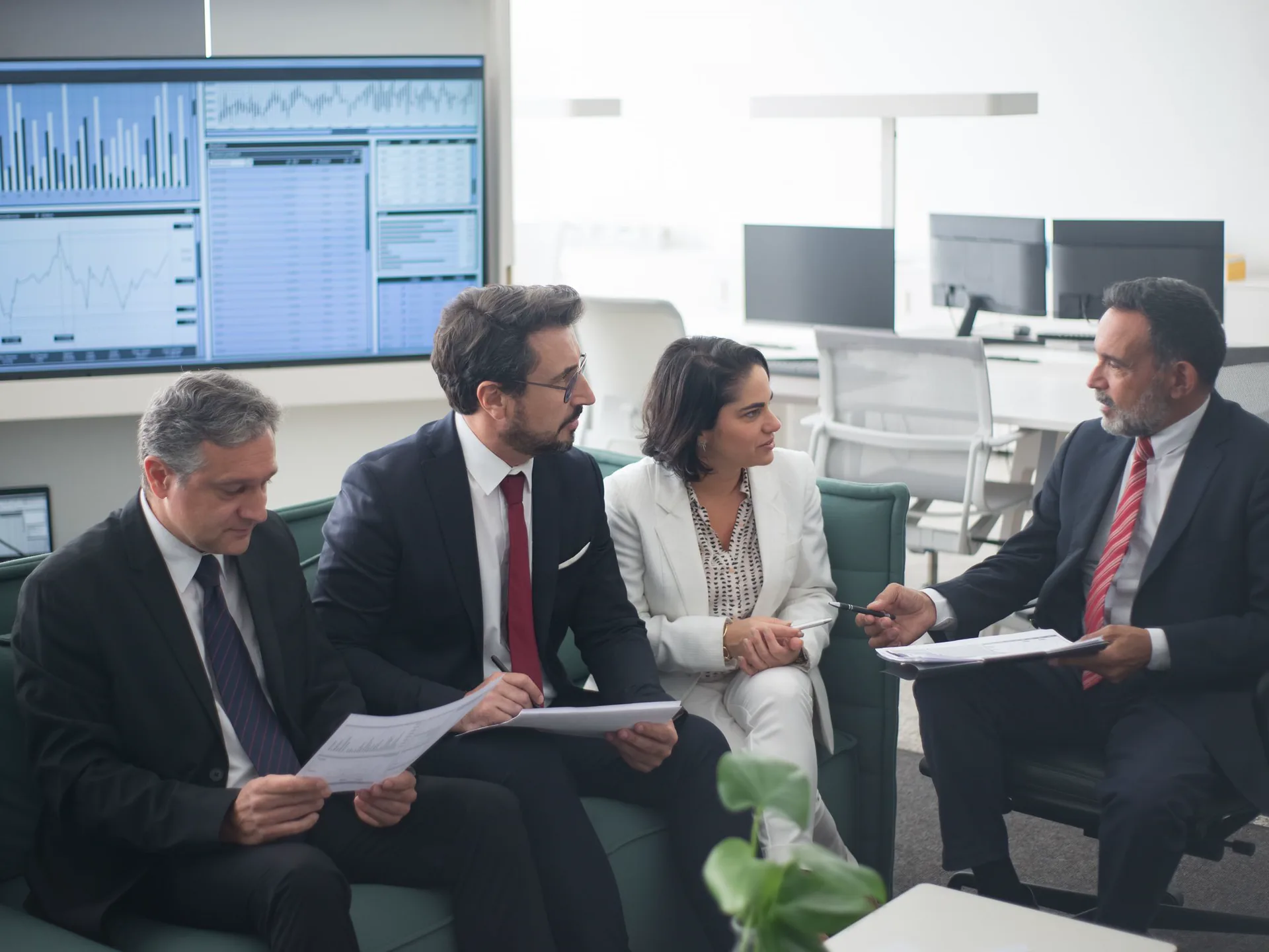 A finance team reviewing figures beside trading desk monitors in an office