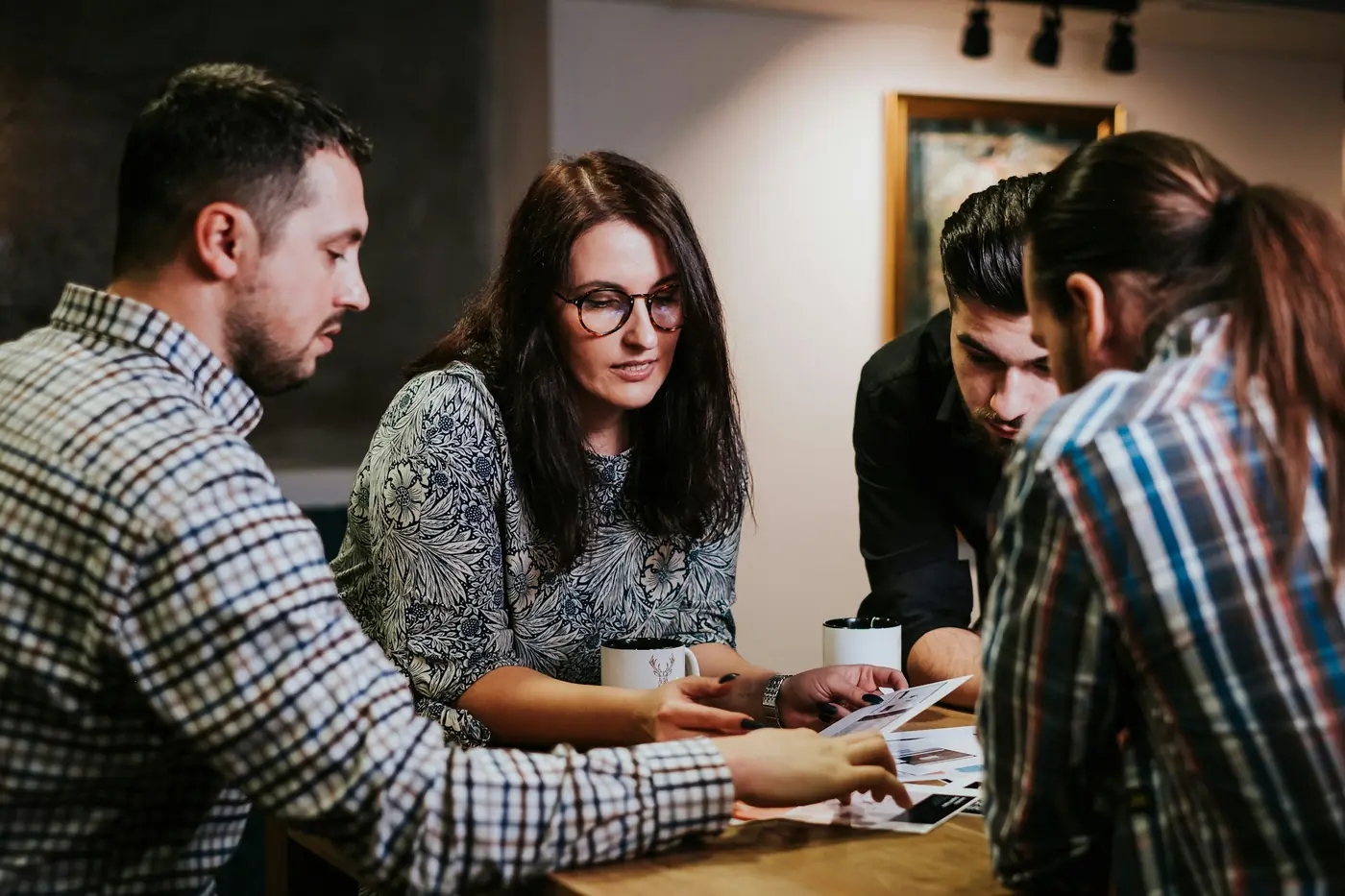 Four colleagues gathered around a wooden table reviewing printed documents together in a warmly lit room