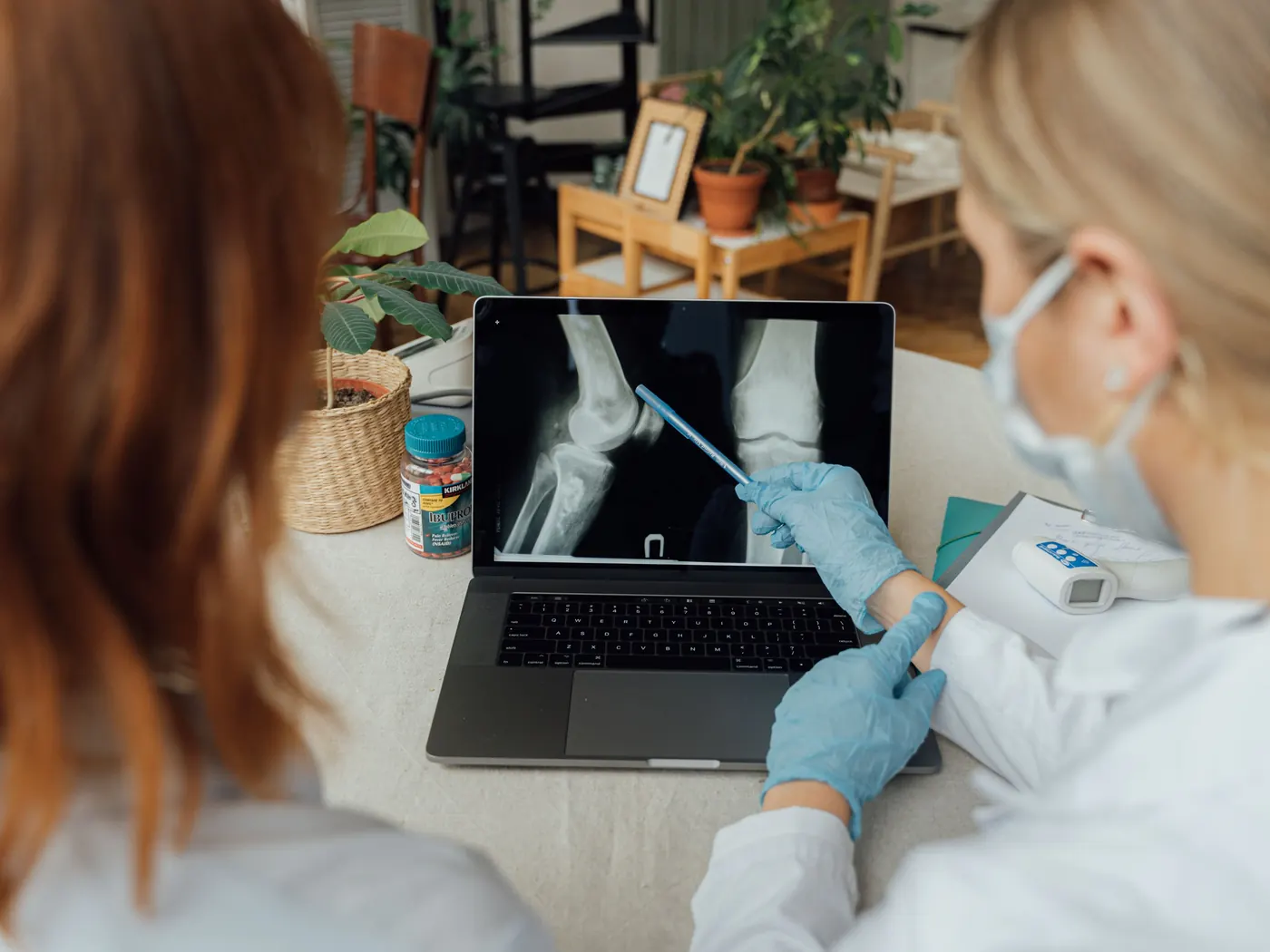 Two doctors reviewing a knee X-ray on a laptop, one pointing at the screen with a pen