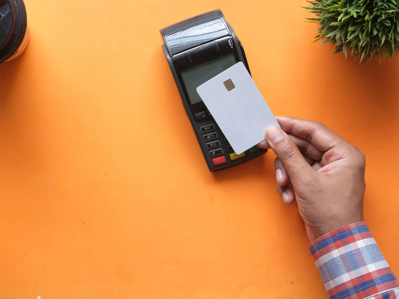 A hand holding a bank card over a card machine on an orange table