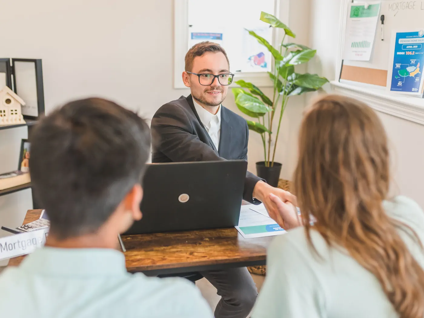 A loan advisor at his desk shaking hands with a couple sitting across from him