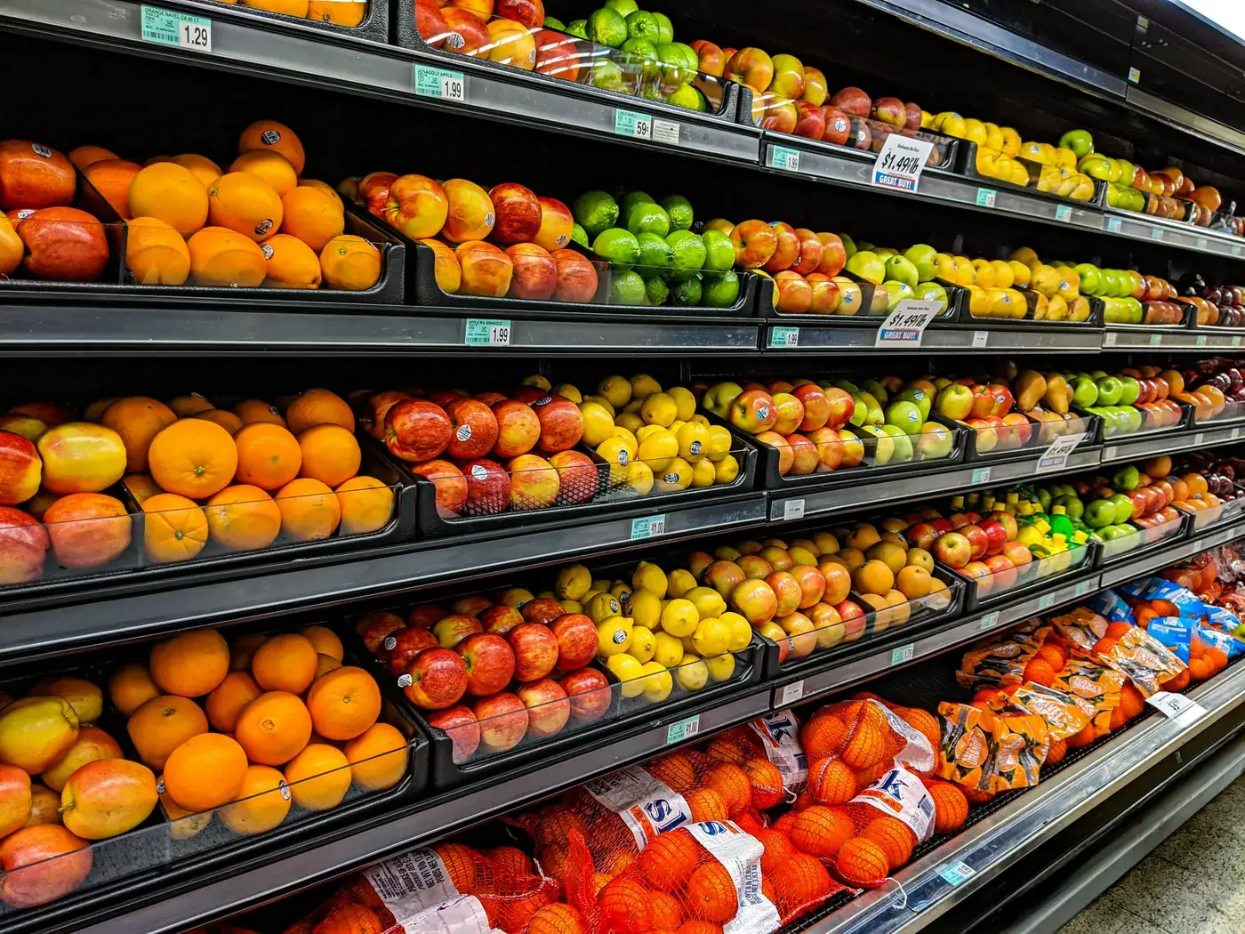 Supermarket shelves full of oranges, apples, lemons and limes, with price labels along each shelf