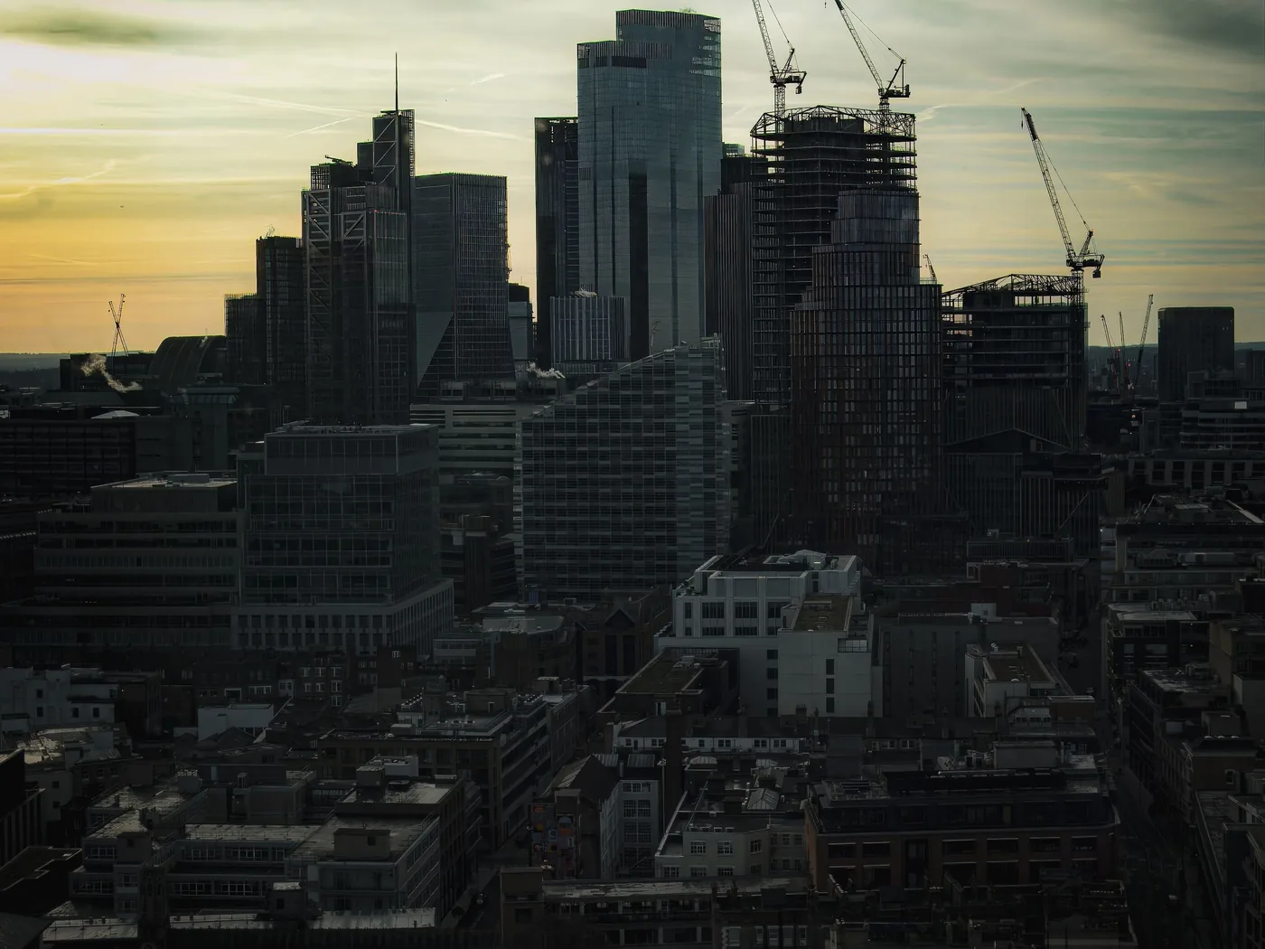 A city skyline at dusk with construction cranes over new towers
