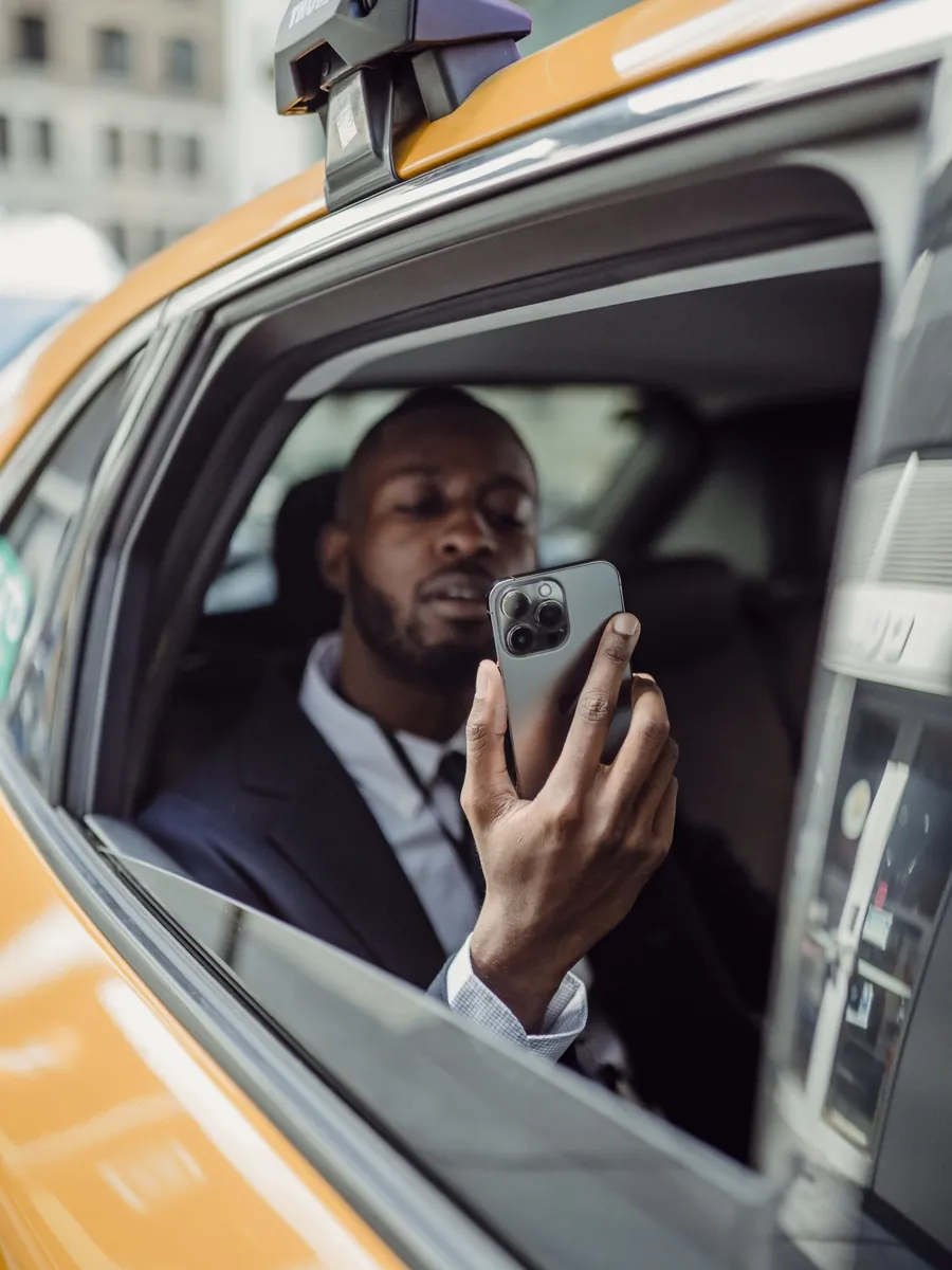A passenger in the back of a taxi checking a phone