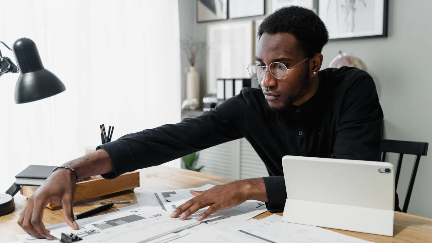 A man at his desk reviewing financial papers next to a tablet