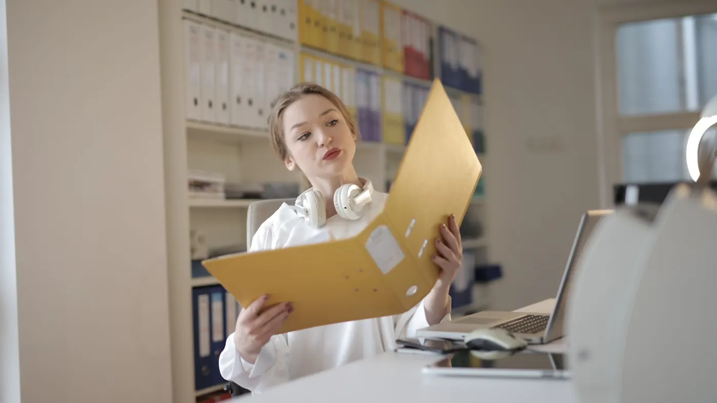 A woman at an office desk reviewing papers in a yellow folder