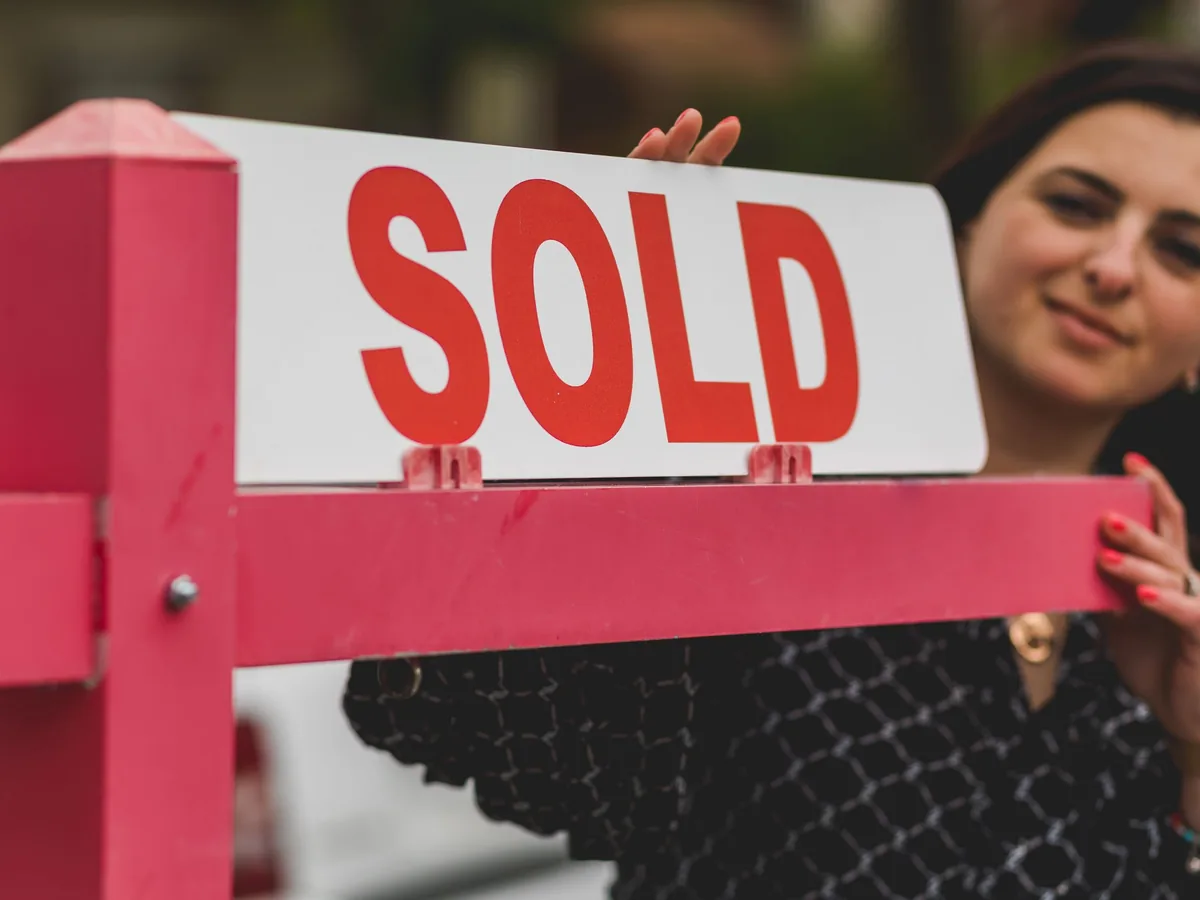 An agent holding a SOLD sign outside a property