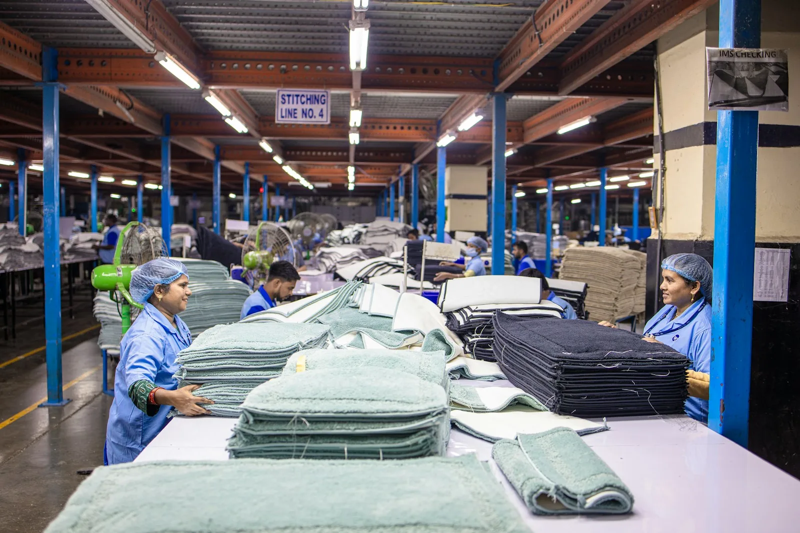 A garment factory stitching line with folded apparel stacked along the benches