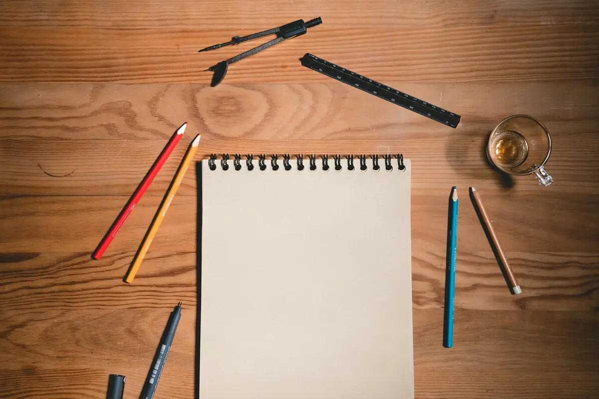 A blank sketch pad surrounded by coloured pencils on a desk
