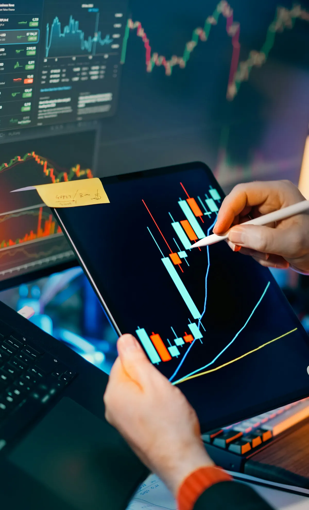 Analyst marking up a forecast chart on a tablet in front of trading screens