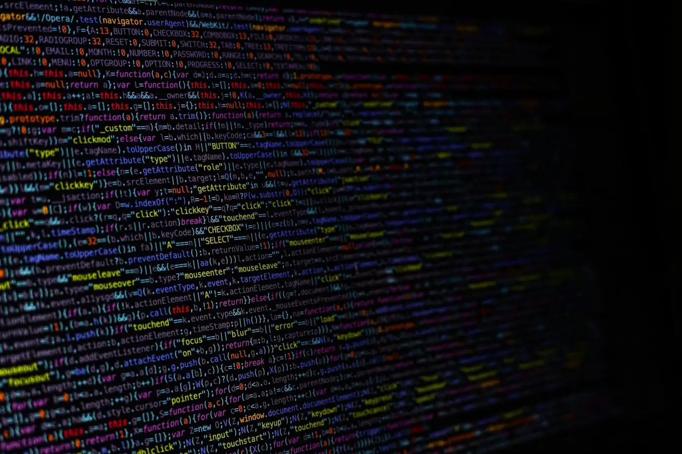 Angled close-up of dense, colourful minified JavaScript code on a dark screen, fading into darkness on the right