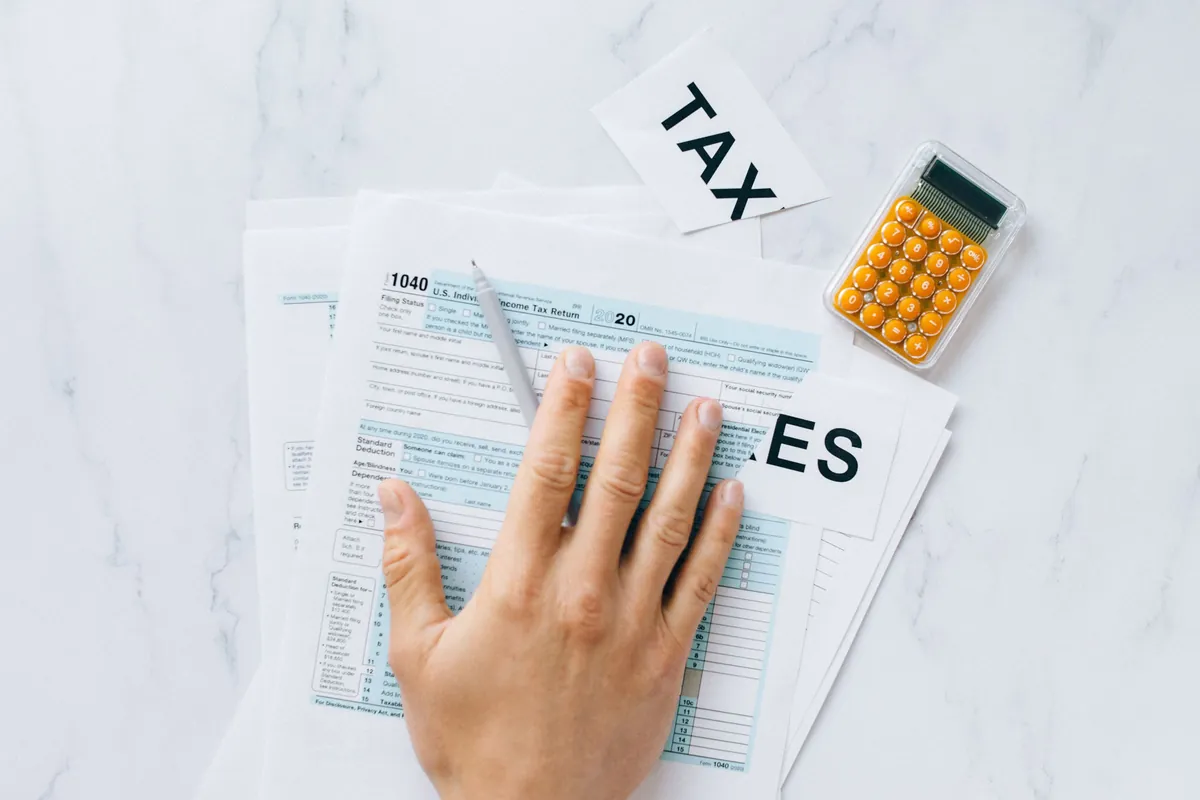 A hand completing a tax return form beside a calculator