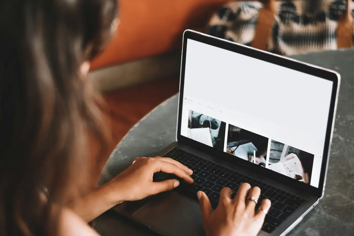 Over-the-shoulder view of a woman typing on a laptop showing a web page with a row of photo thumbnails
