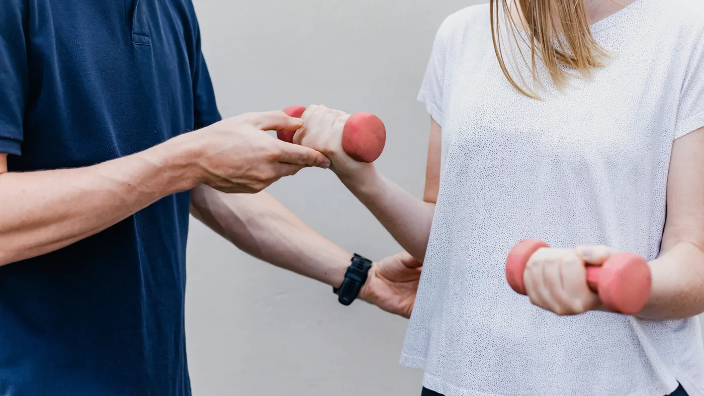 A physiotherapist guiding a patient's arm as she lifts a small dumbbell